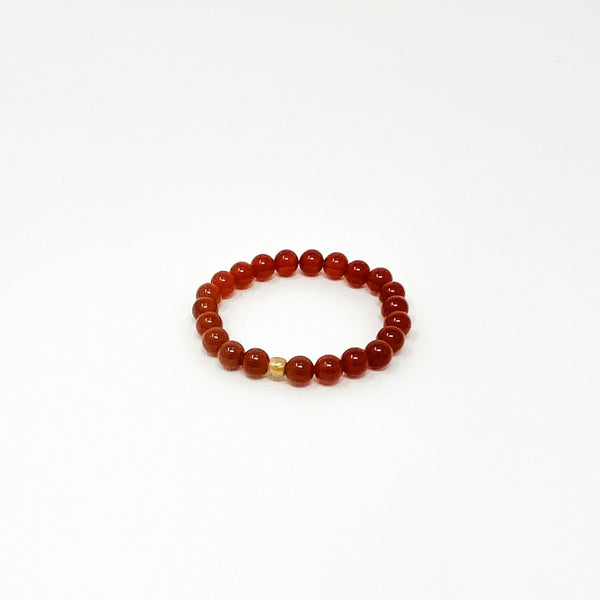 Assorted Satya Bracelets | Satya featuring a single circular bracelet made of polished reddish-brown beads with one small golden bead on a white background.
