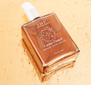 Lustre Drench® Instant Glow Dry Oil | Farmhouse Fresh in a clear glass bottle with shimmering bronze liquid inside, placed on a wet surface with water droplets.