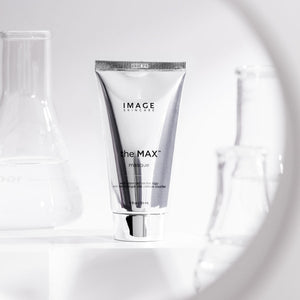 Silver tube of the MAX™ masque | IMAGE Skincare displayed in a clean, bright setting with laboratory glassware in the background, highlighting skincare and wellness.
