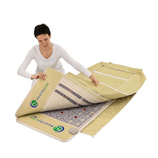 A person unfolding a beige wellness device mat with visible layers and embedded technology, showcasing the TAJ-Mat™ Full 7224 Firm - Photon PEMF InfraMat Pro® | HealthyLine for body care and recovery.