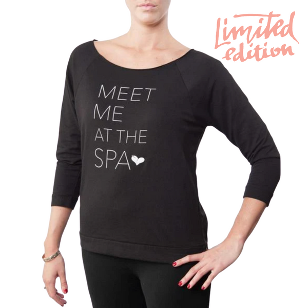 Woman wearing a black "Limited Edition Promotion - Meet Me at the Spa - 3/4 sleeve lightweight sweatshirt | Live Love Spa" with white text and a small heart design, styled casually.