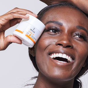 Smiling woman holding a jar of VITAL C hydrating repair crème | IMAGE Skincare near her face, showcasing skincare and hydration for radiant skin.