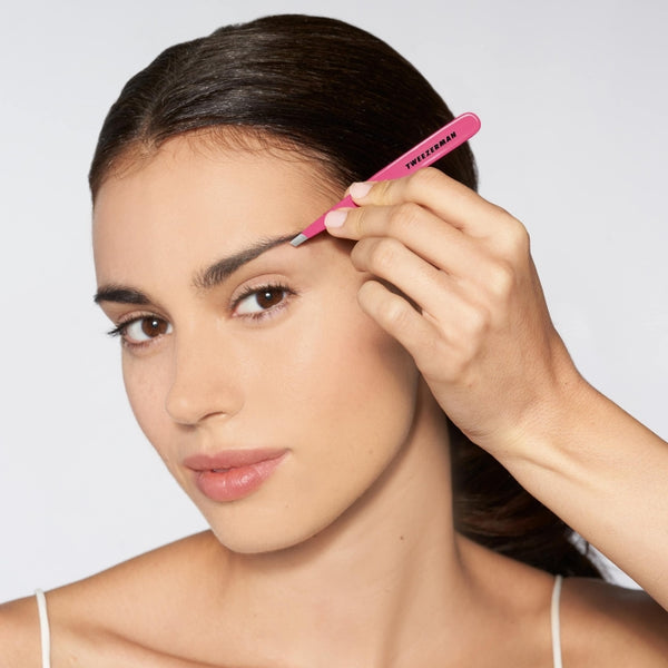 Woman using the pink Slant Tweezer | Tweezerman to shape her eyebrow, demonstrating precise grooming for skincare and beauty care routine.
